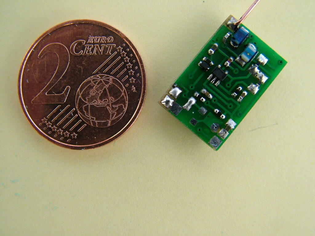 Miniaturowy moduł elektroniczny obok monety 2 eurocentów — porównanie rozmiaru